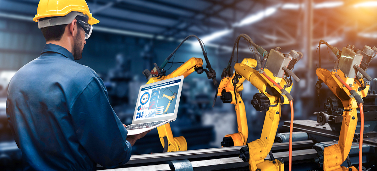 An engineer controls the operations of robotic manufacturing equipment using a laptop.